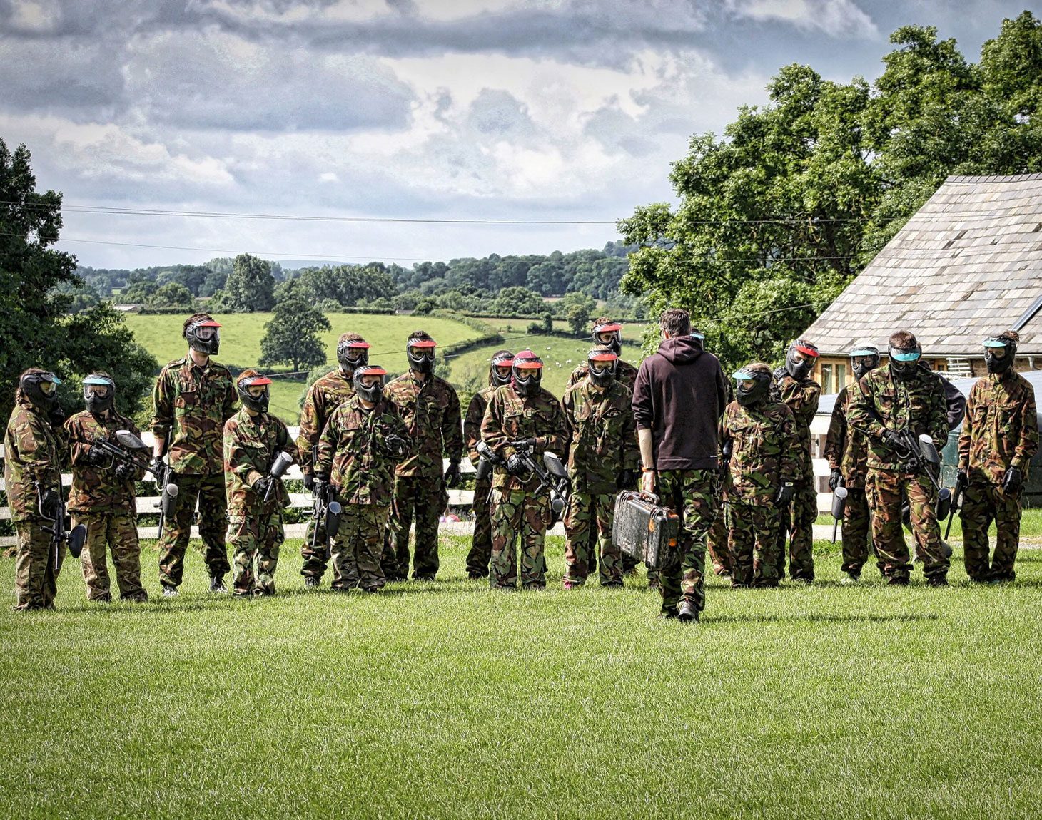 Grupo de pessoas com armamento e roupas para paintball em um gramado verde.